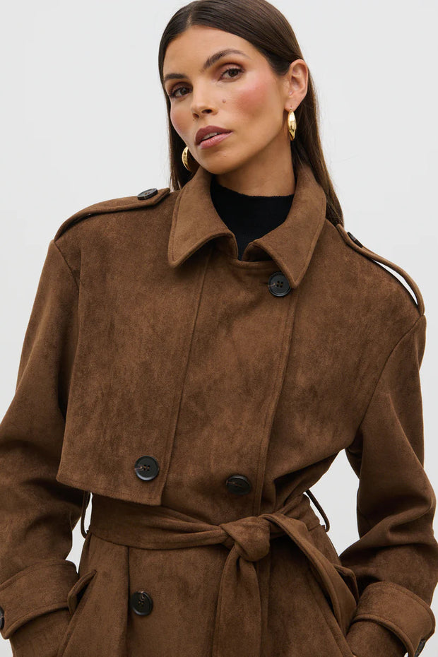 Woman wearing a brown suede coat against a plain background