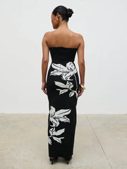 Woman wearing a black strapless dress with white floral patterns on a plain background