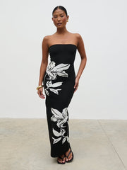 Woman wearing a black strapless dress with white floral patterns on a plain background