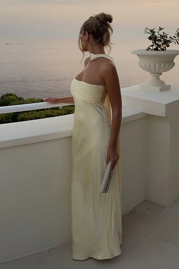 Woman in a strapless dress standing on a balcony overlooking the ocean at sunset.