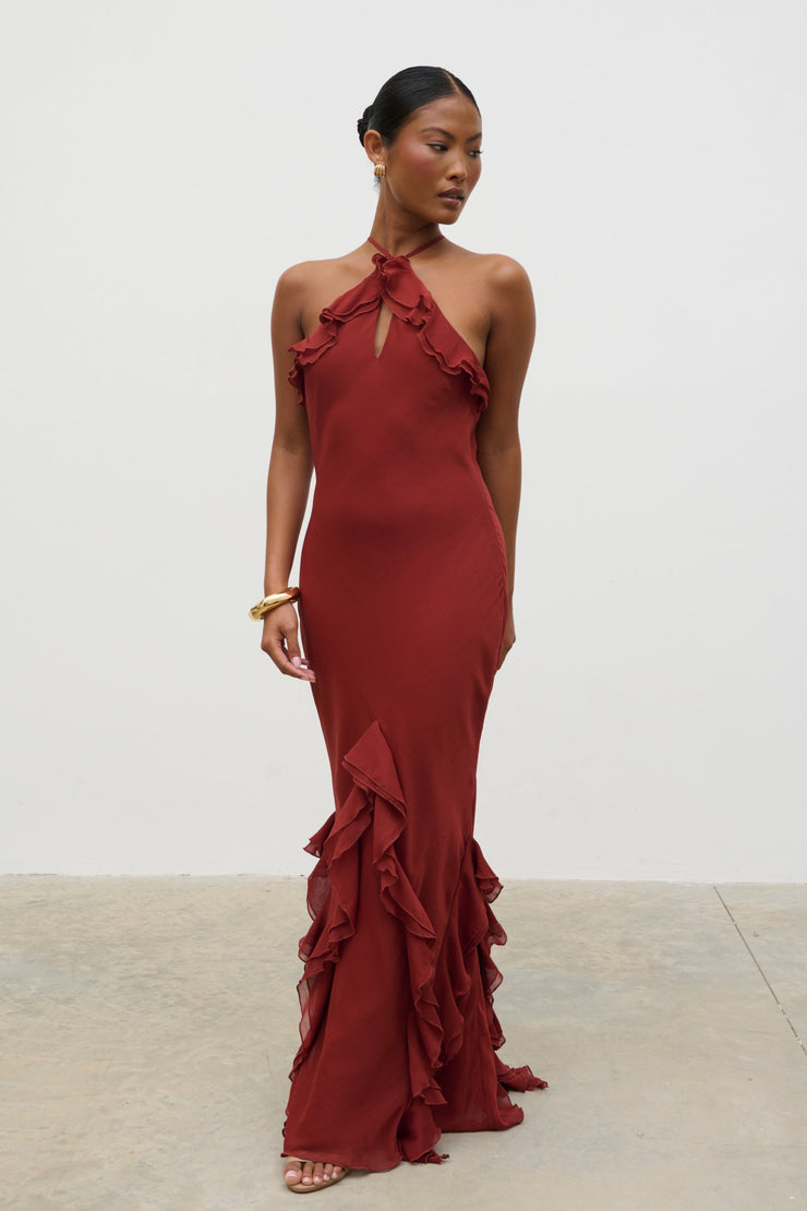 Woman wearing a burgundy evening gown with ruffled details against a white background