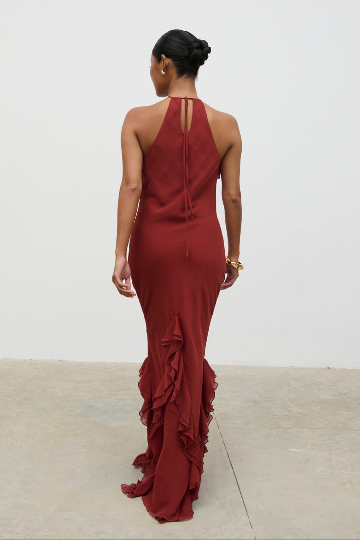 Woman wearing a burgundy evening gown with ruffled details on a plain background